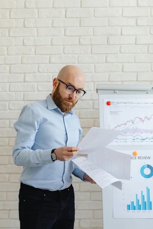 a man standing in front of a white board holding papers, ginger bearded man with glasses, on a desk, insipiring, charts