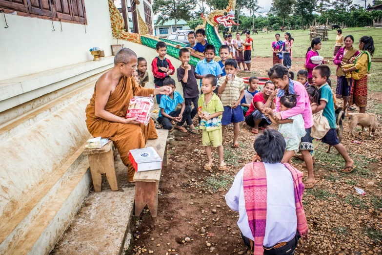 a monk sitting on a bench in front of a group of children, giving gifts to people, thawan duchanee, gopro photo, 15081959 21121991 01012000 4k