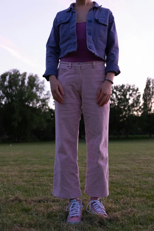 a woman standing on top of a lush green field, an album cover, by Attila Meszlenyi, worn pants, pink and purple, wearing double denim, 33mm photograph