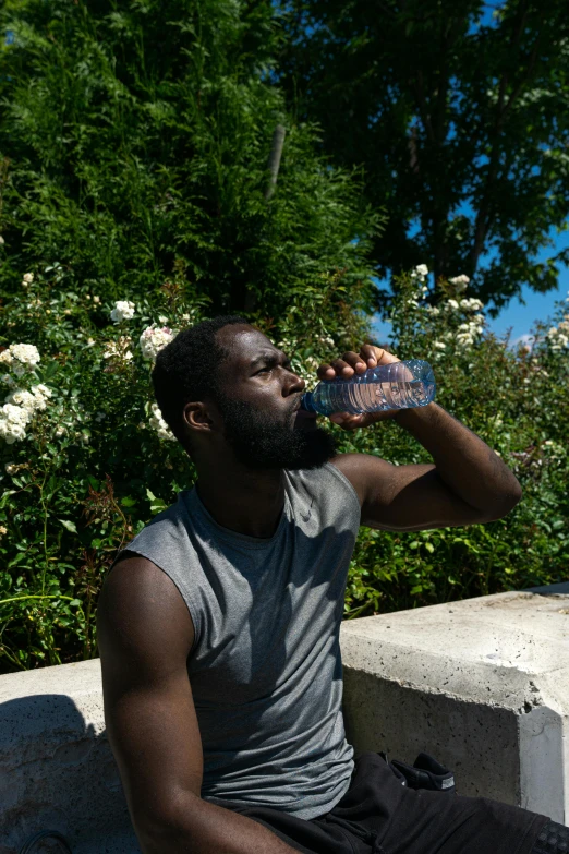 a man sitting on a ledge drinking from a water bottle, pexels contest winner, renaissance, man is with black skin, sunny summer day, lush surroundings, sweaty face