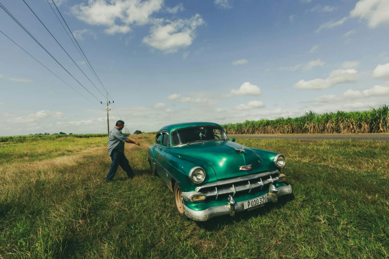 a man standing next to a green car in a field, pexels contest winner, happening, cuban setting, driving a hotrod, annie leibowitz, wide angle”