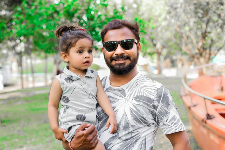 a man holding a little girl in front of a boat, a portrait, by Thota Vaikuntham, pexels contest winner, hurufiyya, wearing shades, avatar image, at a park, graphic print