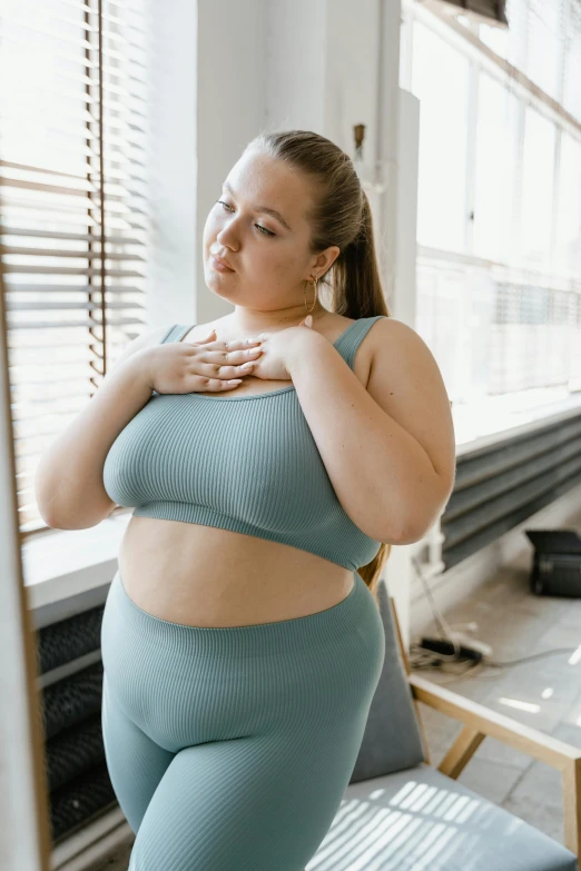 a woman in a blue sports bra top standing in front of a window, trending on pexels, renaissance, obese ), concern, gif, instagram picture