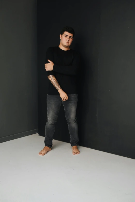 a man standing in front of a black wall, plus-sized, dan dos santos, grey backdrop, studio floor