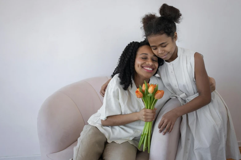 a woman sitting next to a woman holding a bouquet of flowers, sitting on a couch, with a kid, hugging each other, gen z