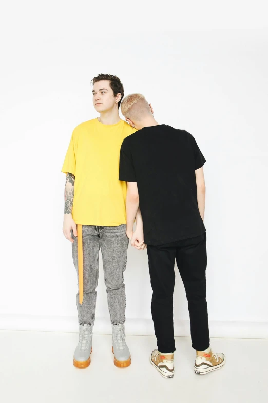 a couple of men standing next to each other, black. yellow, basic clothing, joel fletcher, jeans and t shirt