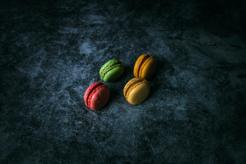 three macarons sitting next to each other on a table, inspired by Charles Le Roux, trending on pexels, visual art, on a dark rock background, red green yellow color scheme, shot with sony alpha 1 camera, a high angle shot