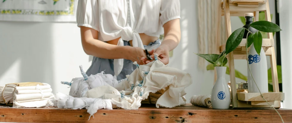 a woman that is standing in front of a table, trending on pexels, process art, cotton fabric, ribbon, recycled, frill