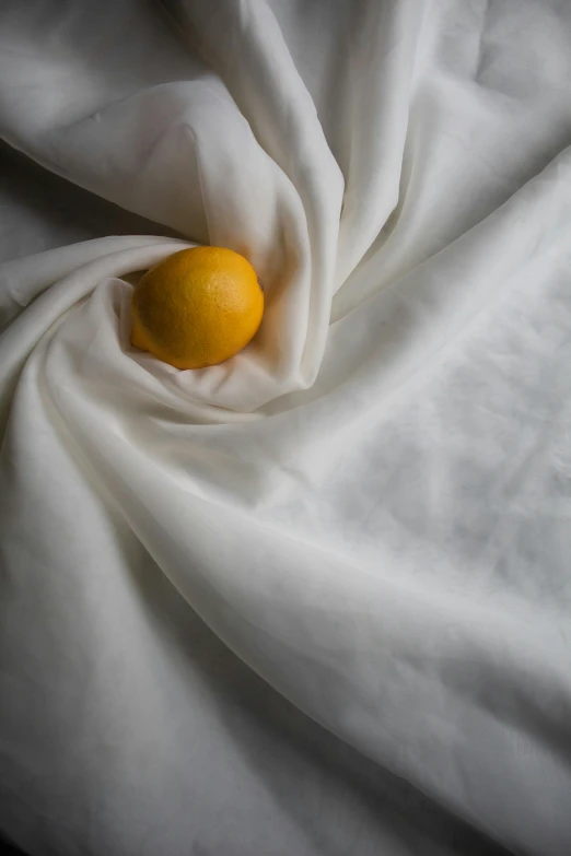 an orange sitting on top of a white sheet, inspired by Li Di, white splendid fabric, close up food photography, silk robes, lemon