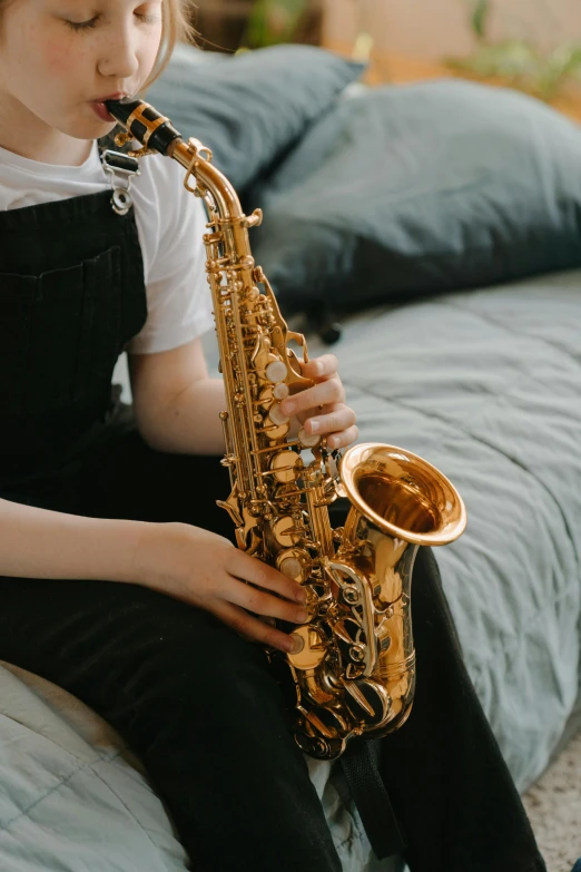 a little girl sitting on a bed playing a saxophone, trending on pexels, australian, neck zoomed in, aged 13, student