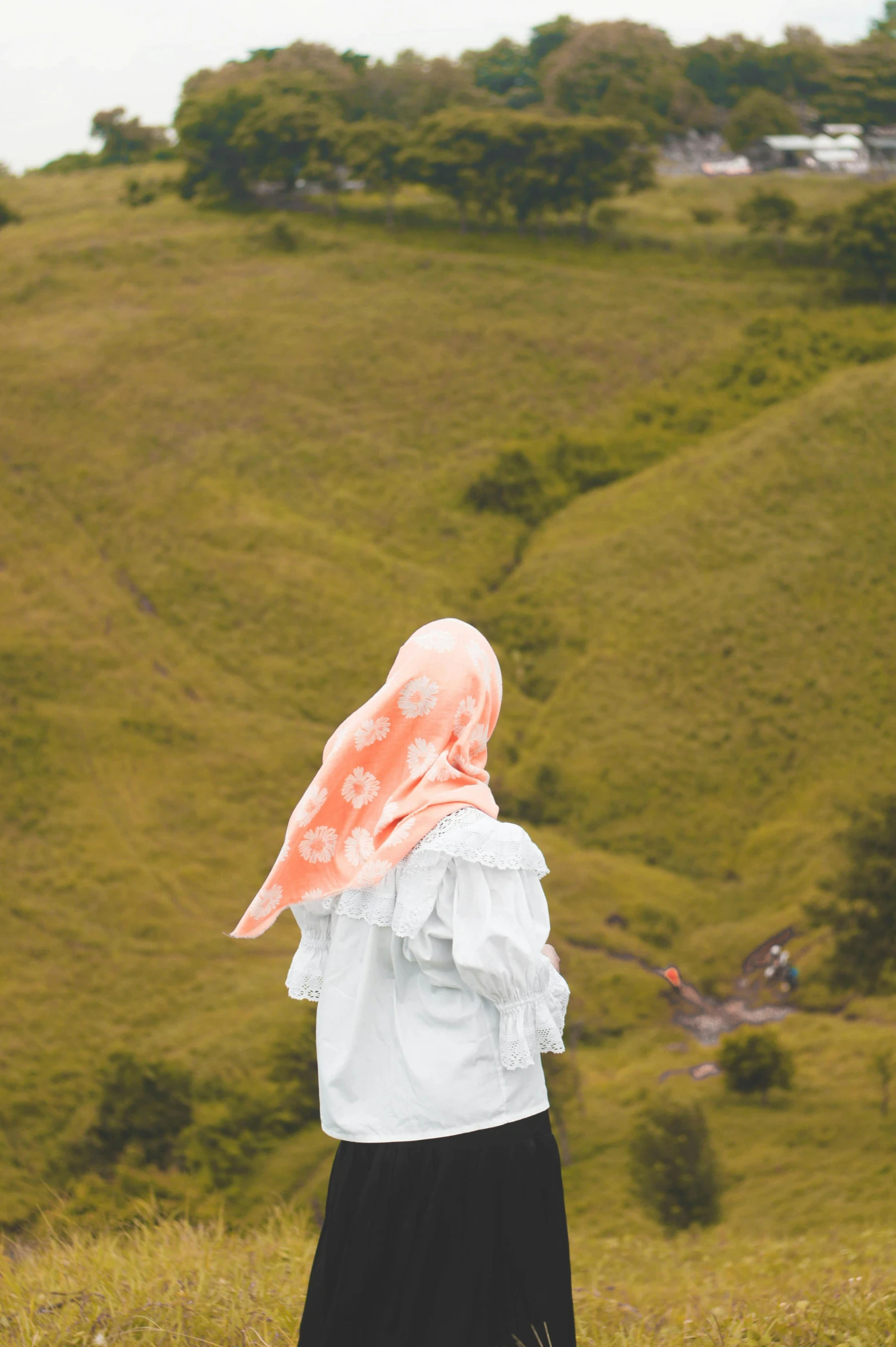 a woman standing on top of a lush green hillside, a colorized photo, by Basuki Abdullah, trending on unsplash, sumatraism, white scarf, covered in coral, looking off into the distance, concert