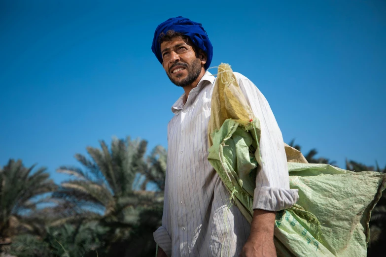 a man wearing a turban and carrying a bag, a portrait, by Scott M. Fischer, pexels contest winner, date palm trees, wearing farm clothes, avatar image, thumbnail