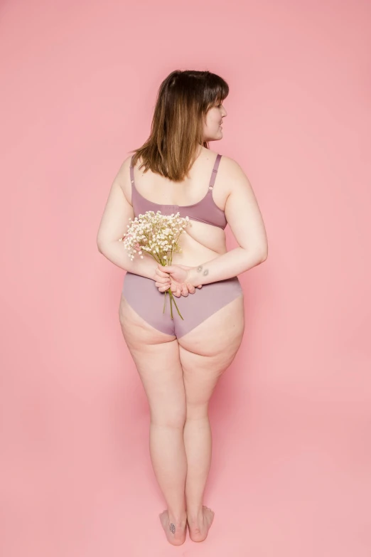 a woman with a bouquet of flowers standing in front of a pink background, by Carey Morris, instagram, shapely toned derriere, fat woman, mauve background, wearing bra