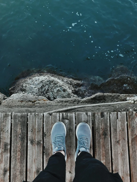 a person standing on a dock next to a body of water, pexels contest winner, sneakers, down there, blue and grey, a photo of the ocean