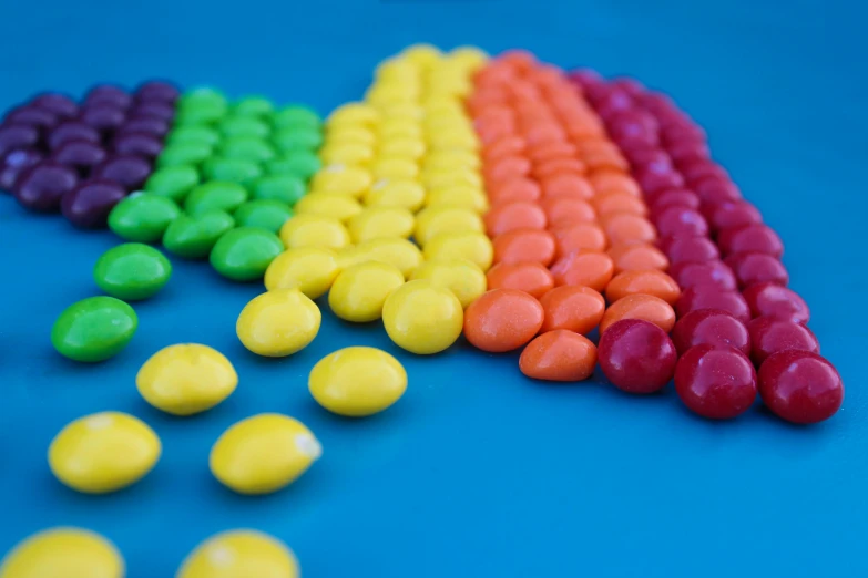 a rainbow of m & m's on a blue surface, an album cover, inspired by Damien Hirst, pexels, corn, gumdrop bunnies, yellow, hdr raytracing
