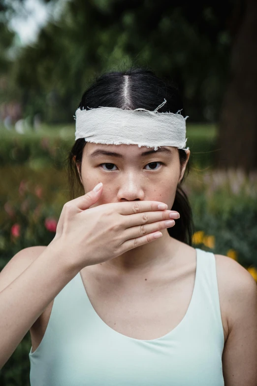 a woman covering her mouth with a bandage, inspired by Ren Hang, pexels contest winner, adventure playground accident, young asian girl, greeting hand on head, ripped fabric