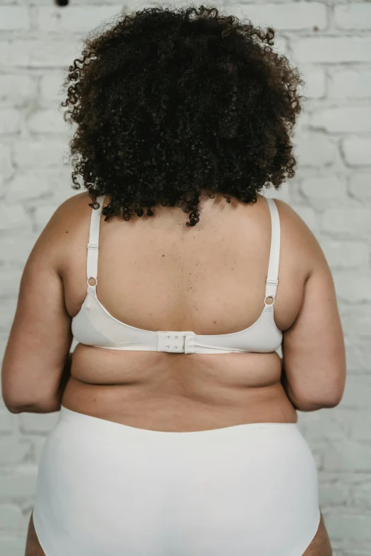 a woman in white underwear standing in front of a brick wall, by Arabella Rankin, unsplash, bra strap, 3 / 4 back view, obese ), detailed product image