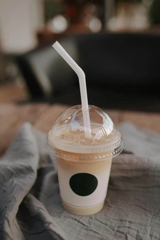 a cup of iced coffee sitting on top of a table, trending on pexels, made of plastic, paul barson, straw, 278122496