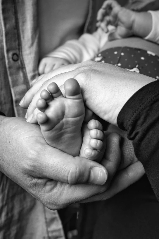 a black and white photo of a person holding a baby's foot, uploaded, beautiful people, digital image, three