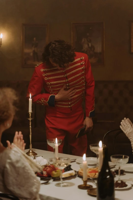 a group of people sitting around a dinner table, an album cover, inspired by Jean-Louis-Ernest Meissonier, pexels contest winner, rococo, red uniform, 2 0 2 1 cinematic 4 k framegrab, skinny male magician, feels good man