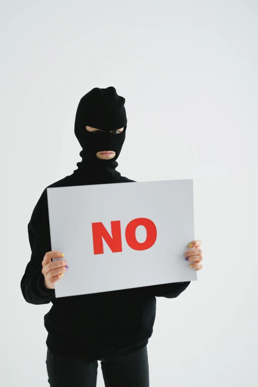 a man in a black mask holding a no sign, trending on pexels, high-key, non-binary, crimes, no hoodie