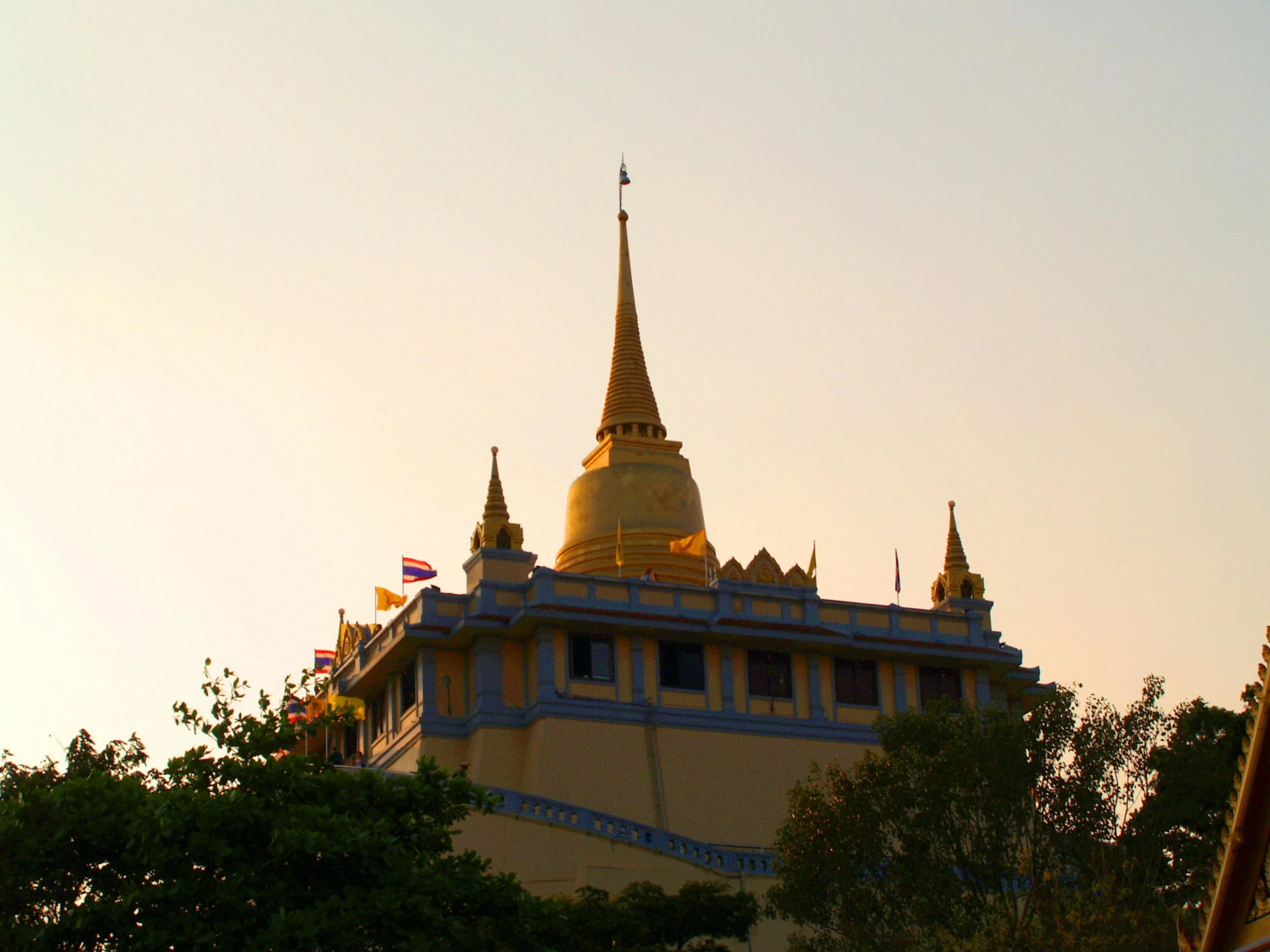 a yellow and blue building surrounded by trees, a picture, inspired by Yerkaland, unsplash, samikshavad, thai temple, pink golden hour, spire, thumbnail