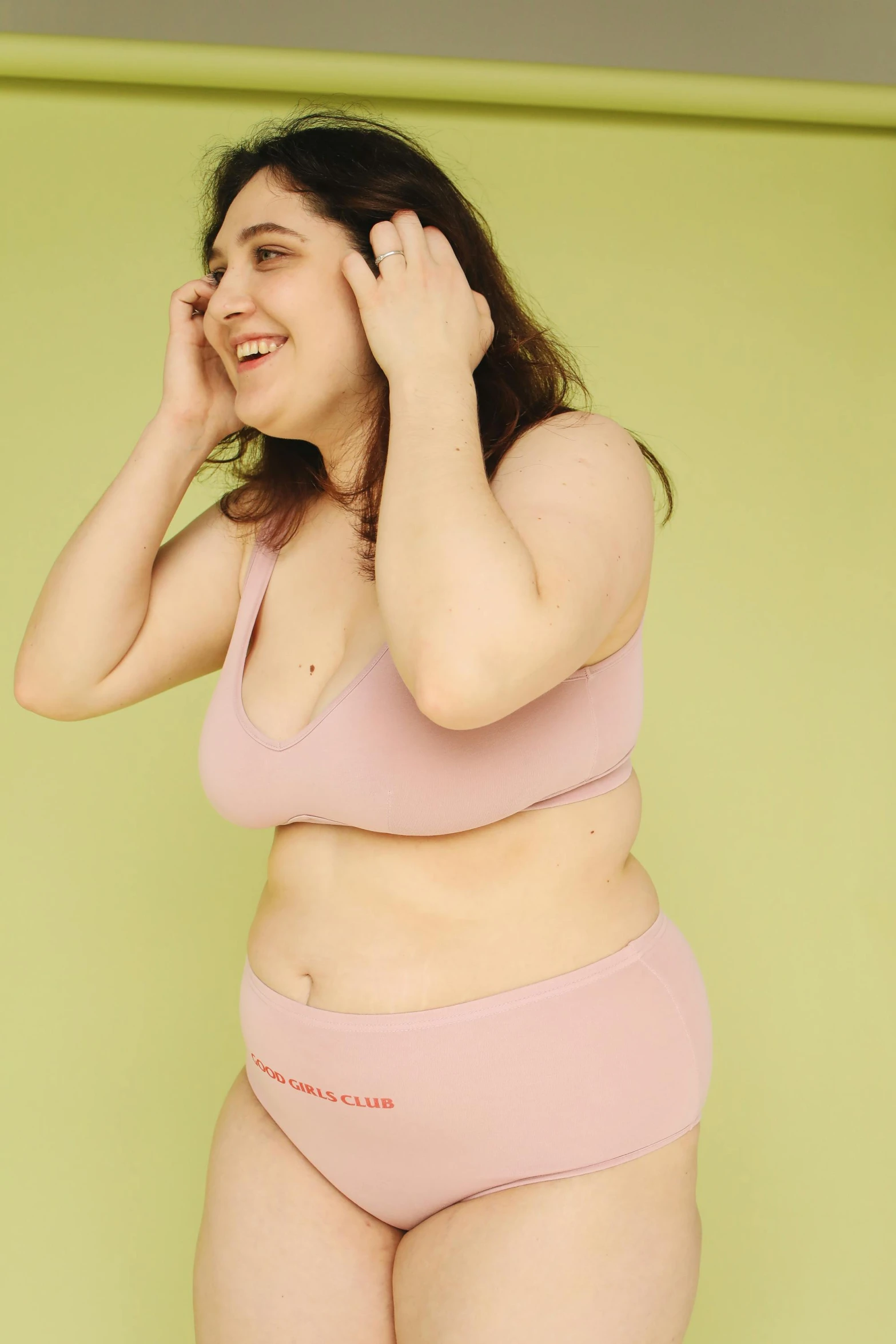 a woman in a pink underwear standing in front of a green wall, by Anita Malfatti, unsplash, happening, plus-sized, pale pink bikini, on a pale background, looking from side!