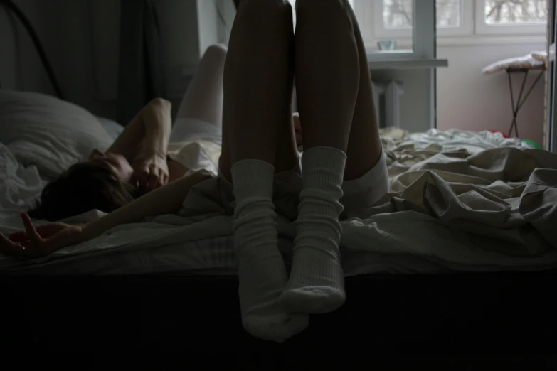 a woman laying on top of a bed next to a window, inspired by Elsa Bleda, pexels contest winner, aestheticism, wearing skirt and high socks, dark and white, couple on bed, painful