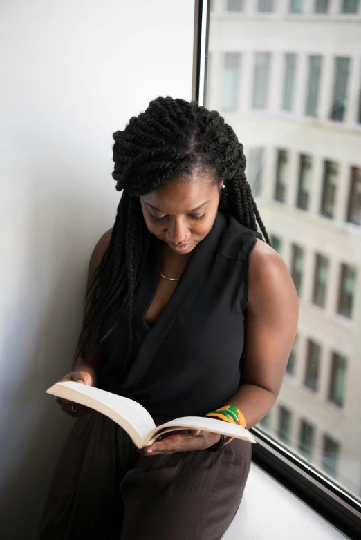 a woman sitting on a window sill reading a book, by Stokely Webster, long black braids, in an office, promo image, teaching