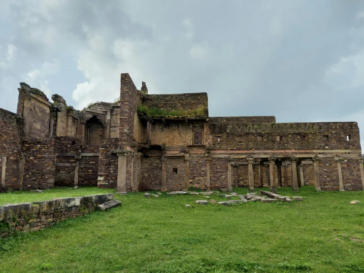 a large stone building sitting on top of a lush green field, pexels contest winner, romanesque, indore, roman bath, collapsed buildings, background image