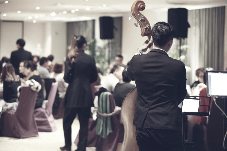 a man playing a cello in a room full of people, unsplash, gentlemens dinner, 3 jazz musicians, formal wear, thumbnail