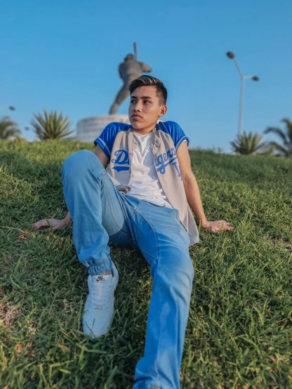 a man sitting on top of a lush green field, an album cover, unsplash, realism, blue pants, from egypt, he is about 20 years old | short, eloy morales
