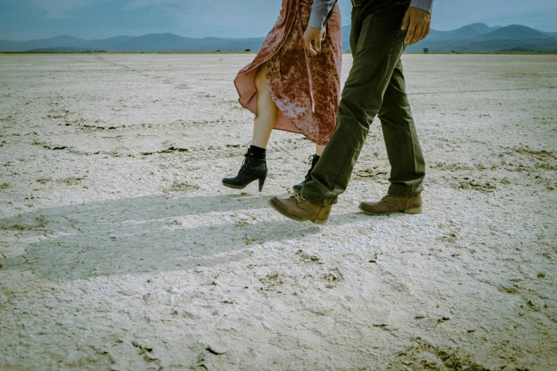 a man and a woman walking in the desert, an album cover, by Lee Loughridge, pexels contest winner, close-up on legs, detailed product image, dry dirt, background image