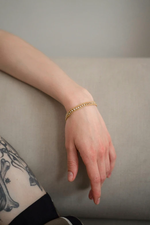 a woman sitting on a couch with a tattoo on her arm, by Nina Hamnett, gold bracelet, product photograph, square, south east asian with long