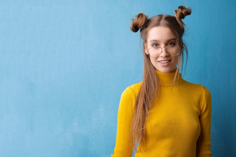 a woman standing in front of a blue wall, inspired by Jean-Étienne Liotard, trending on pexels, brown hair in two buns, colors: yellow, nerdy, wearing turtleneck