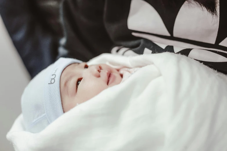 a woman holding a baby wrapped in a blanket, by Emma Andijewska, pexels contest winner, wan adorable korean face, extremely handsome, wearing a white hospital gown, wearing a cute hat