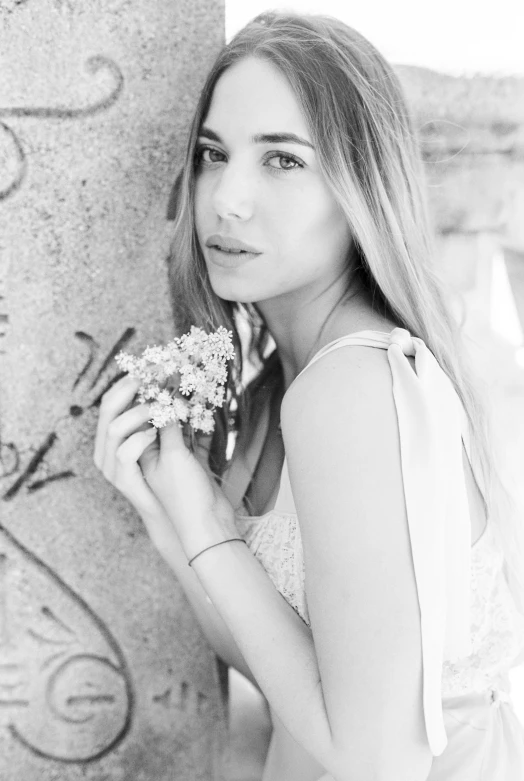 a woman leaning against a pillar with a flower in her hand, a black and white photo, inspired by Anna Boch, 🤤 girl portrait, gypsophila, portrait of ana de armas, a cute young woman