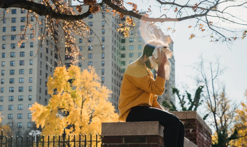 a person sitting on a brick wall smoking a cigarette, a photo, by Ellen Gallagher, pexels contest winner, fall foliage, a man wearing golden mask, city views, on a yellow canva