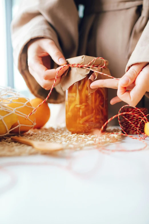 a close up of a person holding a jar of food, process art, orange ribbons, netting, packaging design, vine