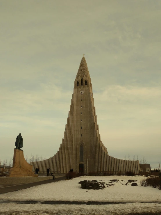 a very tall building with a statue in front of it, a statue, inspired by Þórarinn B. Þorláksson, unsplash, brutalism, very long spires, marilyn church h, an icelandic landscape, album cover