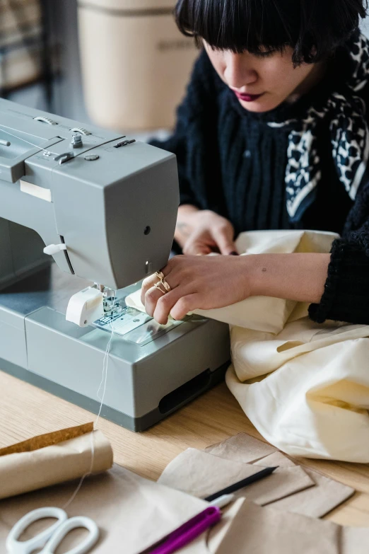 a woman is working on a sewing machine, inspired by Sarah Lucas, trending on unsplash, folds of fabric, architect, digitally remastered, high quality product photo