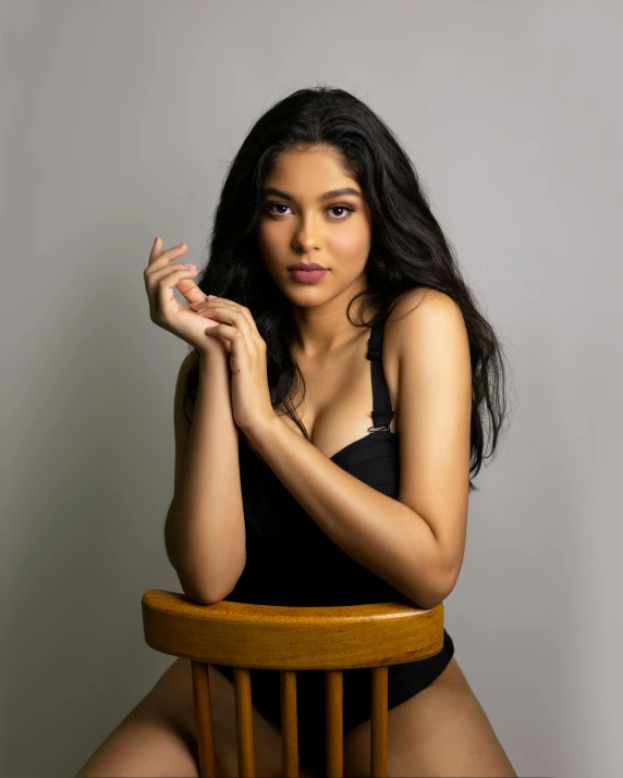 a woman sitting on top of a wooden chair, by Robbie Trevino, long curvy black hair, asher duran, actress, proud looking