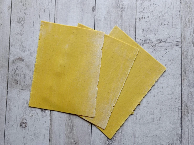 four pieces of yellow paper sitting on top of a wooden table, inspired by Géza Dósa, private press, textured parchment background, cheddar, dust, 2 1 0 mm