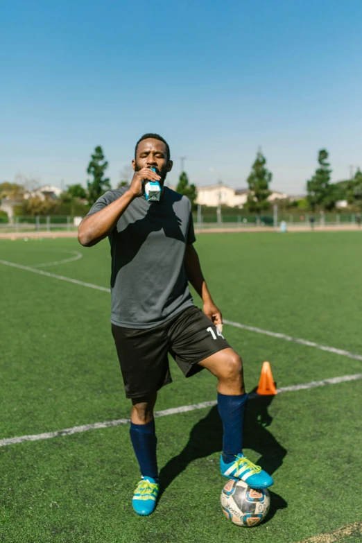 a man standing on top of a soccer field, drinking cough syrup, taken on iphone 14 pro, athletic muscle tone, yawning