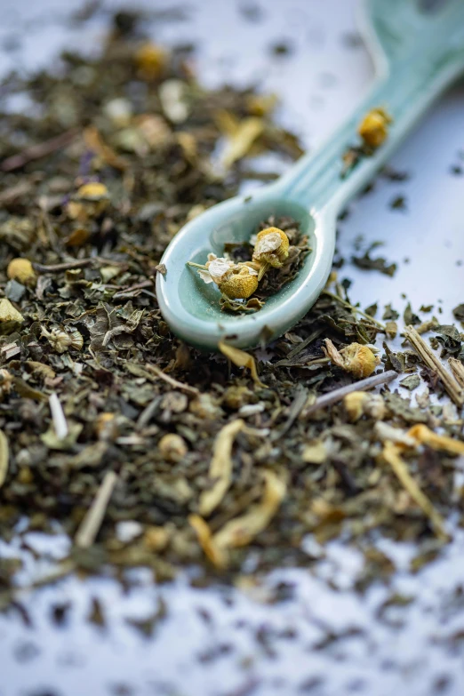 a spoon filled with dried herbs sitting on top of a table, green tea, zoomed in, slide show, tall shot