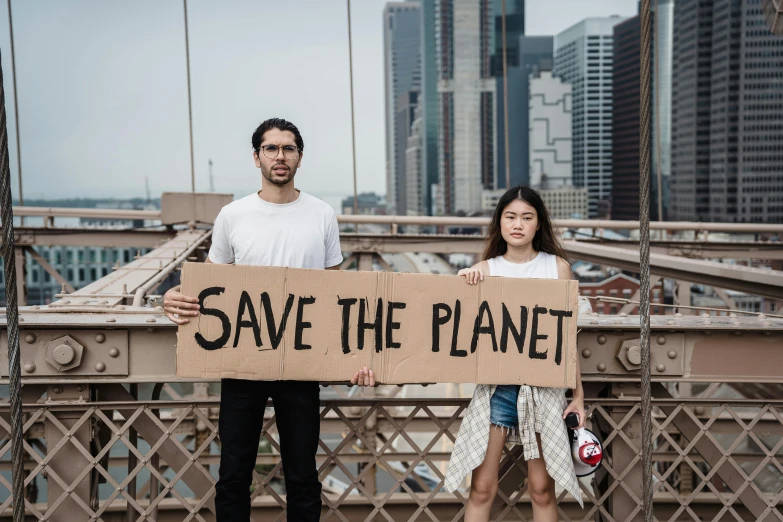a man and a woman holding a sign that says save the planet, by Jakob Gauermann, pexels contest winner, standing on a bridge, sydney hanson, avatar image, julia fuentes