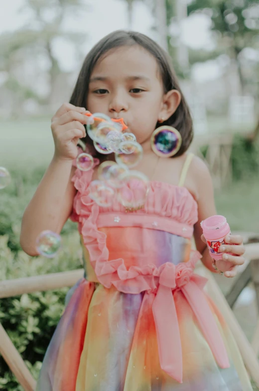 a little girl that is standing in front of a fence, iridescent soapy bubbles, wearing a pink dress, snacks, dressed in a beautiful