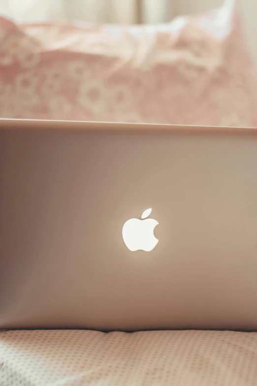 a laptop computer sitting on top of a bed, a digital rendering, inspired by Emma Ríos, pexels, romanticism, apple logo, pearlescent skin, smooth pink skin, back lighting