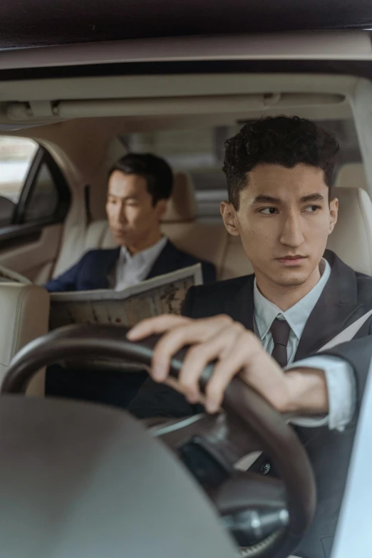 a man in a suit sitting in the driver's seat of a car, an album cover, inspired by Zhang Xiaogang, pexels contest winner, photorealism, two young men, alessio albi and shin jeongho, performance, looking distracted