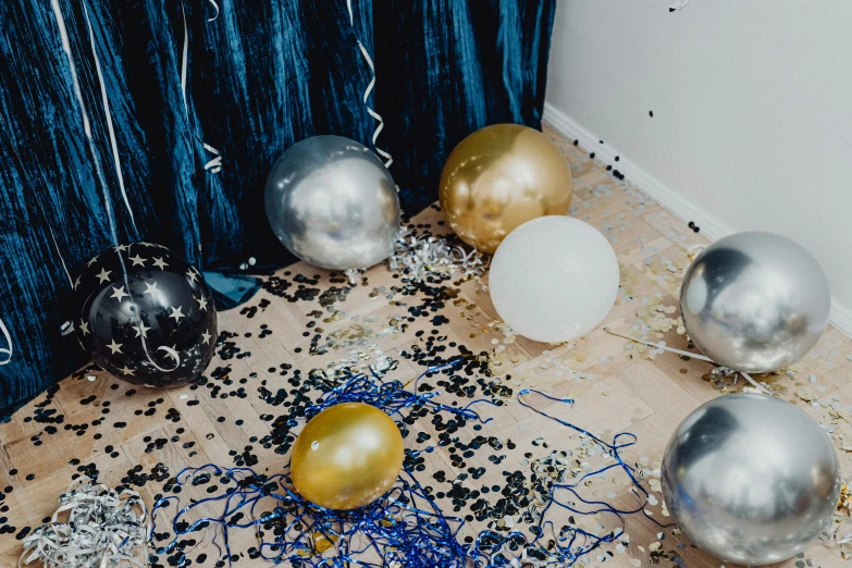 a table topped with lots of balloons and confetti, by Julia Pishtar, trending on unsplash, blue silver and black, curtain bangs, debris on the floor, gold and indigo